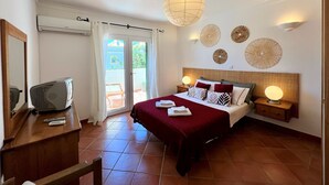 A hotel room with a bed, bedside lamps, a ceiling fan, a desk with a computer, and a sliding glass door to the outside. - Casa D`sul by Homing (Tavira)