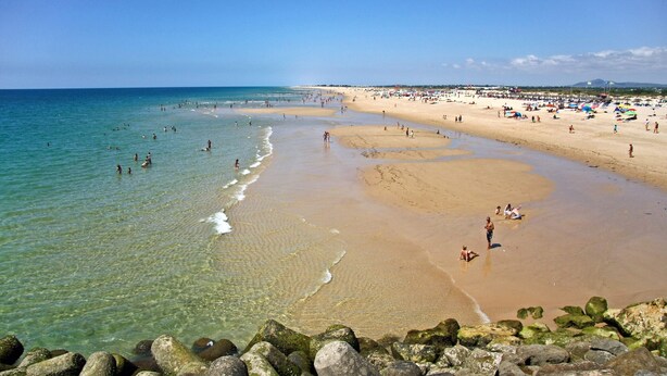 A beach with clear water, sandy shore, and rocks in the foreground. - Casa D`sul by Homing (Tavira)