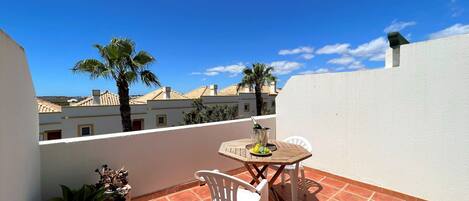 A terrace with a table and chairs, potted plants, and a view of buildings and palm trees.
