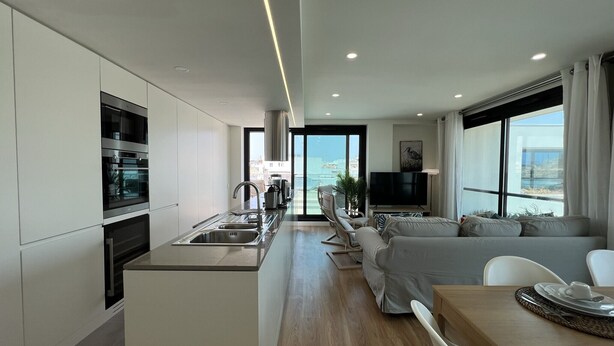Een moderne keuken met inbouwapparatuur, een eethoek met tafel en stoelen, en een woonkamer met een bank en televisie.