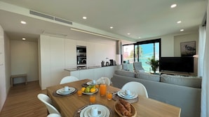 Een moderne keuken met inbouwapparatuur, een eetgedeelte met ontbijtset en een woonruimte met uitzicht op zee.