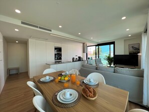 Eine moderne Küche mit integrierten Geräten, ein Essbereich mit Frühstücksutensilien und ein Wohnbereich mit Blick auf das Meer.