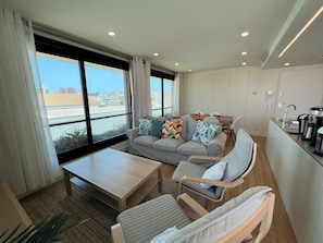 A modern living room with a sofa, a coffee table, and a dining area. - Faro Design 3 by Homing (Faro)