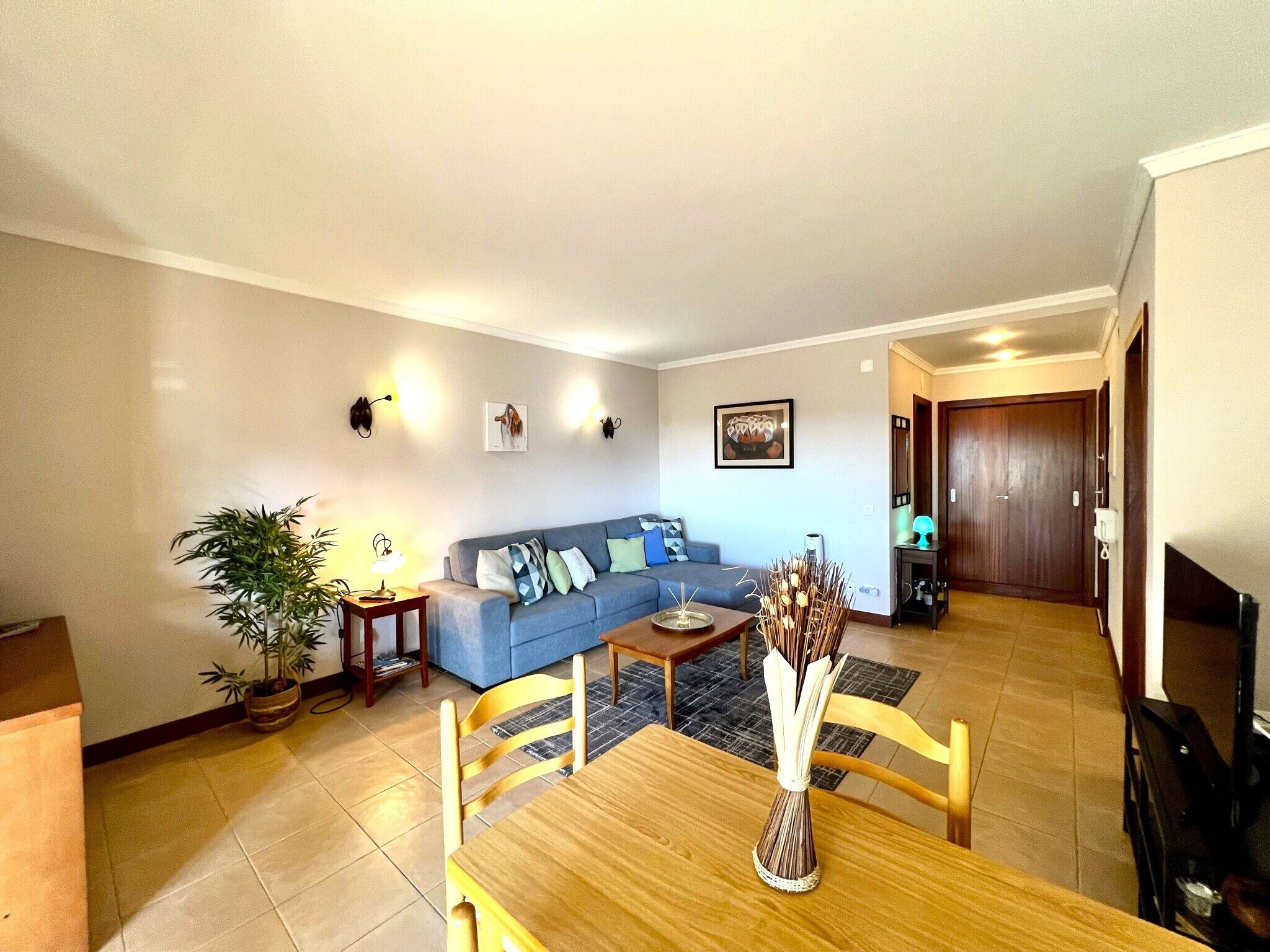A living room with a sofa, a dining table with chairs, a potted plant, and a vase.