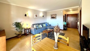 A living room with a sofa, a dining table with chairs, a potted plant, and a vase. - Albufeira Salgados Beach 3 by Homing (Albufeira)