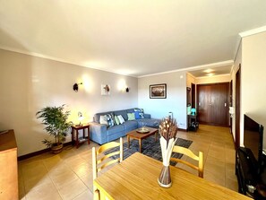 A living room with a sofa, a dining table with chairs, a potted plant, and a vase. - Albufeira Salgados Beach 3 by Homing (Albufeira)