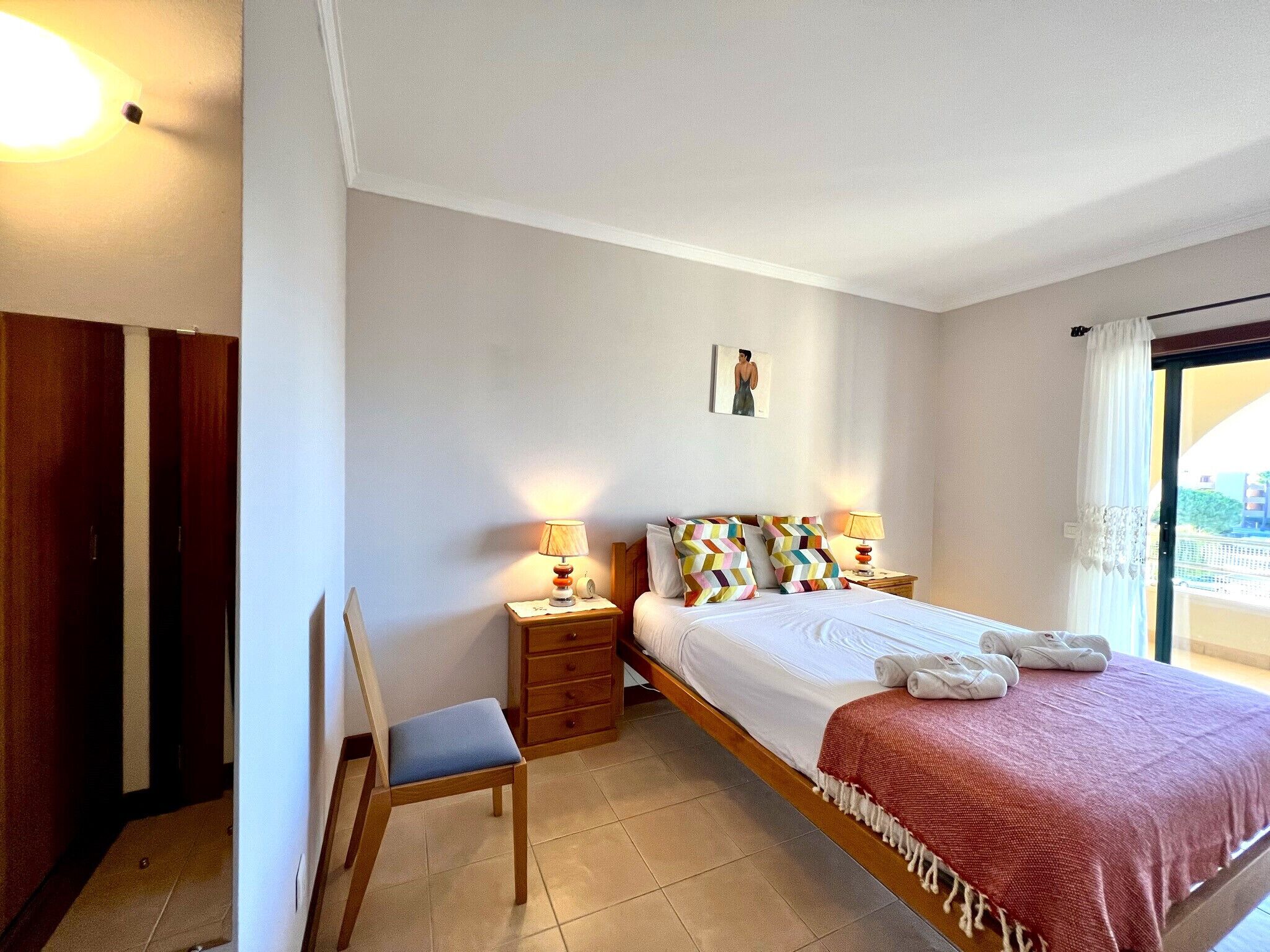 A hotel room with a bed, a chair, a nightstand, and a window with curtains.