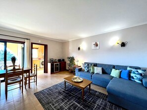 A living room with a blue sofa, a wooden coffee table, and a dining area with a table and chairs. - Albufeira Salgados Beach 3 by Homing (Albufeira)