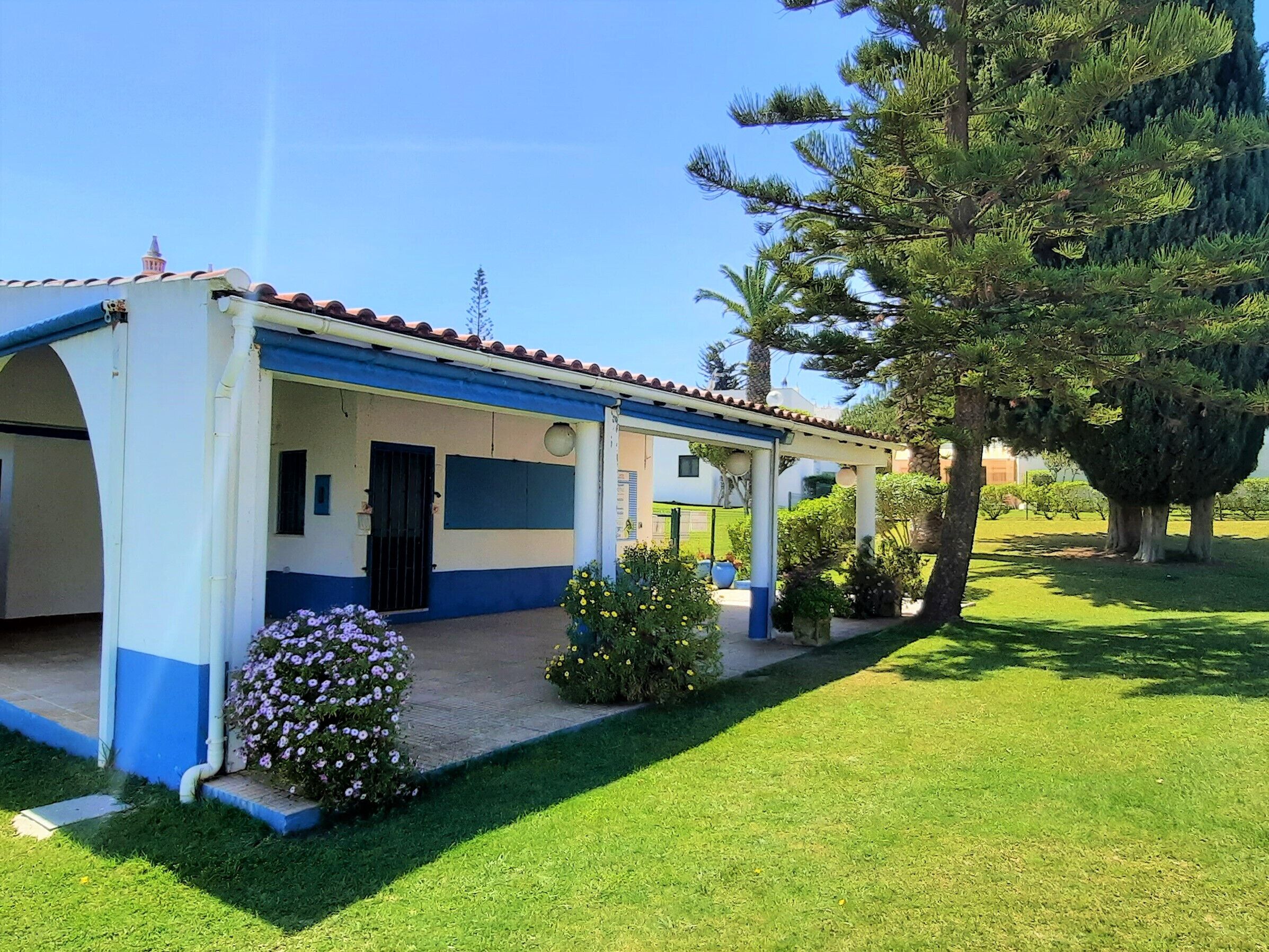 A two-story building with a blue and white exterior, a covered patio area, and a well-maintained lawn with flowering plants.