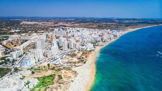 Eine Vogelperspektive einer Küstenstadt mit dichter Hochhausbebauung, einem Sandstrand und einem klaren, blauen Meer.