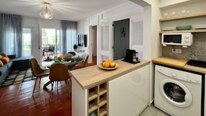 Eine moderne Küche mit integriertem Waschtrott, ein Essbereich mit Tisch und Stühlen sowie ein Wohnzimmer mit Sofa und Fernseher.