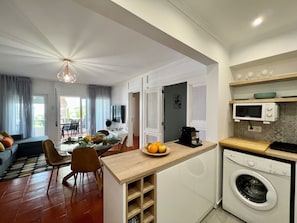 A modern kitchen with a built-in washing machine, a dining area with a table and chairs, and a living room with a sofa and a TV. - Armação DE Pêra Brightness 2 With Pool (Lagoa)