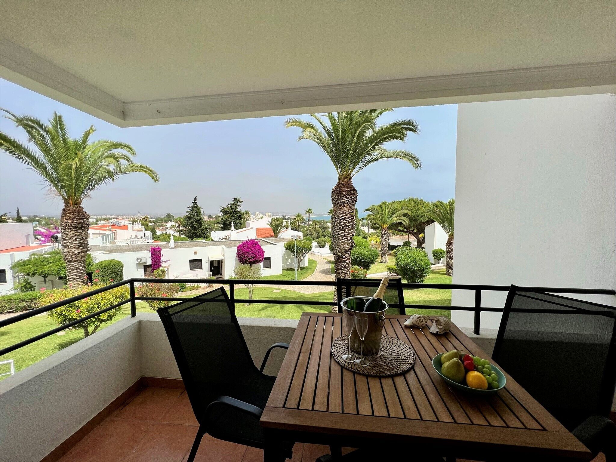 A balcony with a table set for two, a bottle of champagne, and a bowl of fruit.