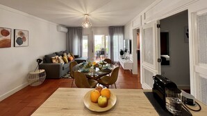 Ein modernes Wohnzimmer mit Essbereich, mit einem Holztisch mit Obst, einer Couch mit Kissen und einer Kaffeemaschine.