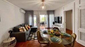 Ein modernes Wohnzimmer mit Essbereich, einer Couch mit Kissen, einem runden Couchtisch und einem an der Wand montierten Fernseher.