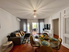 A modern living room with a dining area, a sofa with cushions, a round coffee table, and a TV mounted on the wall. - Armação DE Pêra Brightness 2 With Pool (Lagoa)
