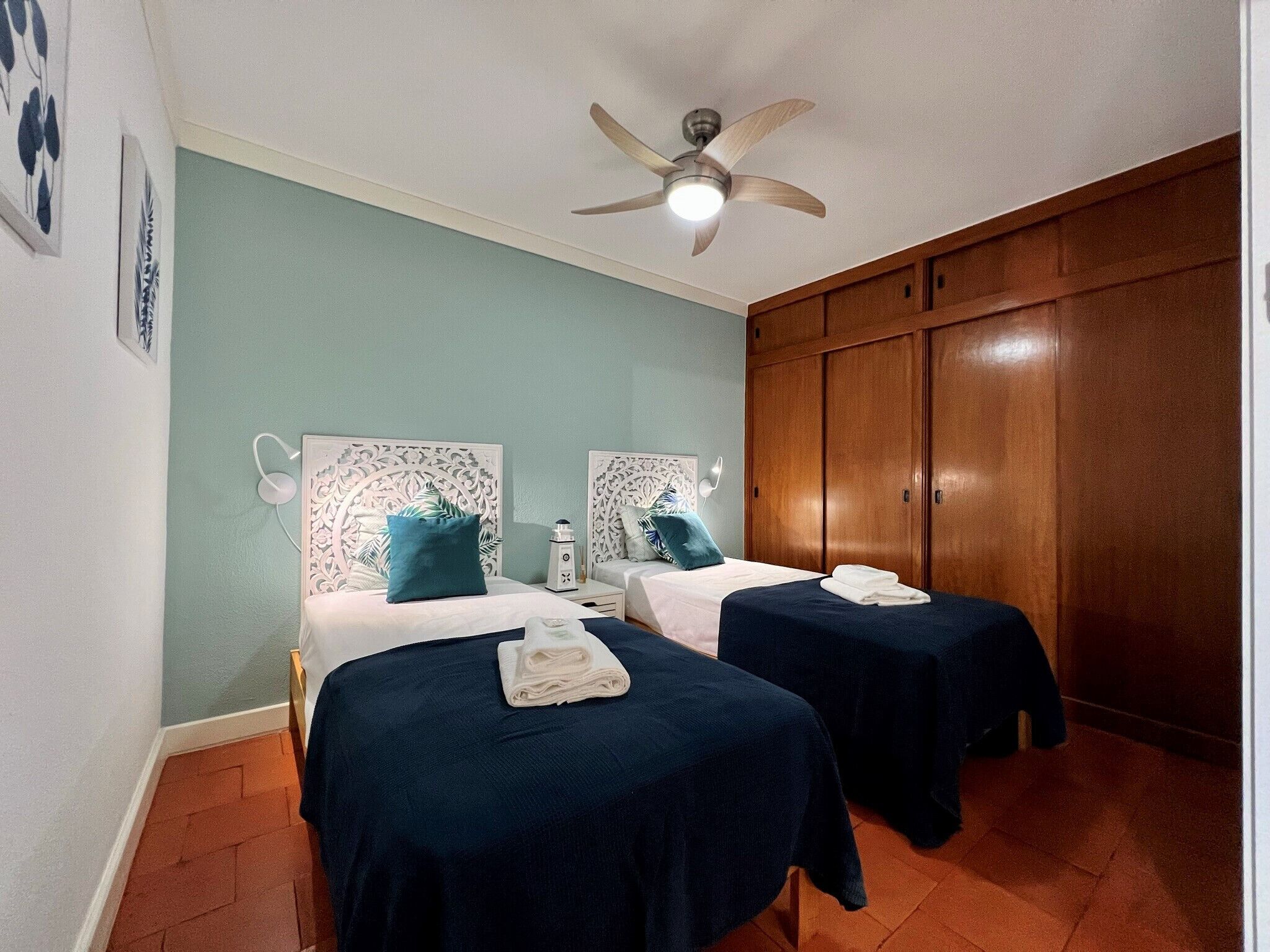 A room with two beds, a ceiling fan, and wooden wardrobes.