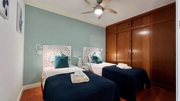 A room with two beds, a ceiling fan, and wooden wardrobes.