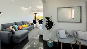 A modern living room with a grey sofa, a coffee table, and two armchairs. There is a large mirror on the wall and a potted plant. - Albufeira Central 2 by Homing (Albufeira)