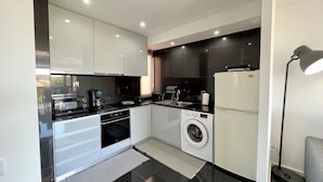 A modern kitchen with white cabinets, a black countertop, a built-in oven, a washing machine, and a refrigerator. - Albufeira Central 2 by Homing (Albufeira)