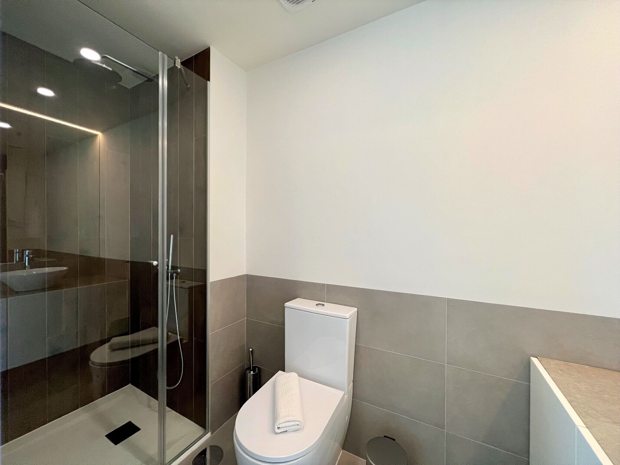 Un bagno moderno con cabina doccia in vetro, un water bianco e un lavandino.