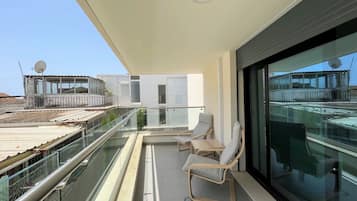 A balcony with glass railings, two lounge chairs, and a view of the cityscape.