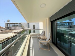 Ein Balkon mit Glasgeländern, zwei Liegestühlen und Blick auf die Stadtlandschaft.