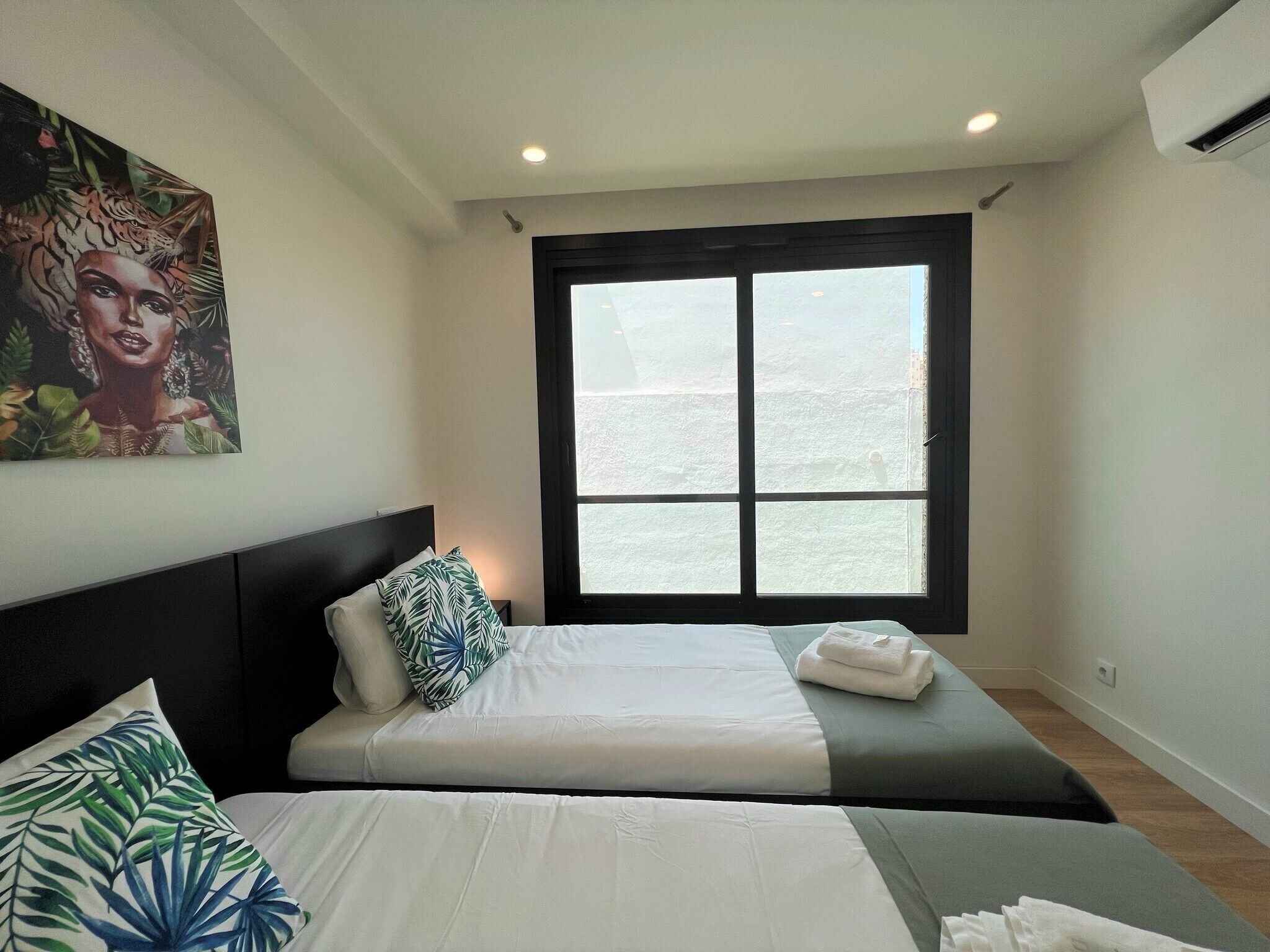 A hotel room with two beds, a large window, and a painting on the wall.