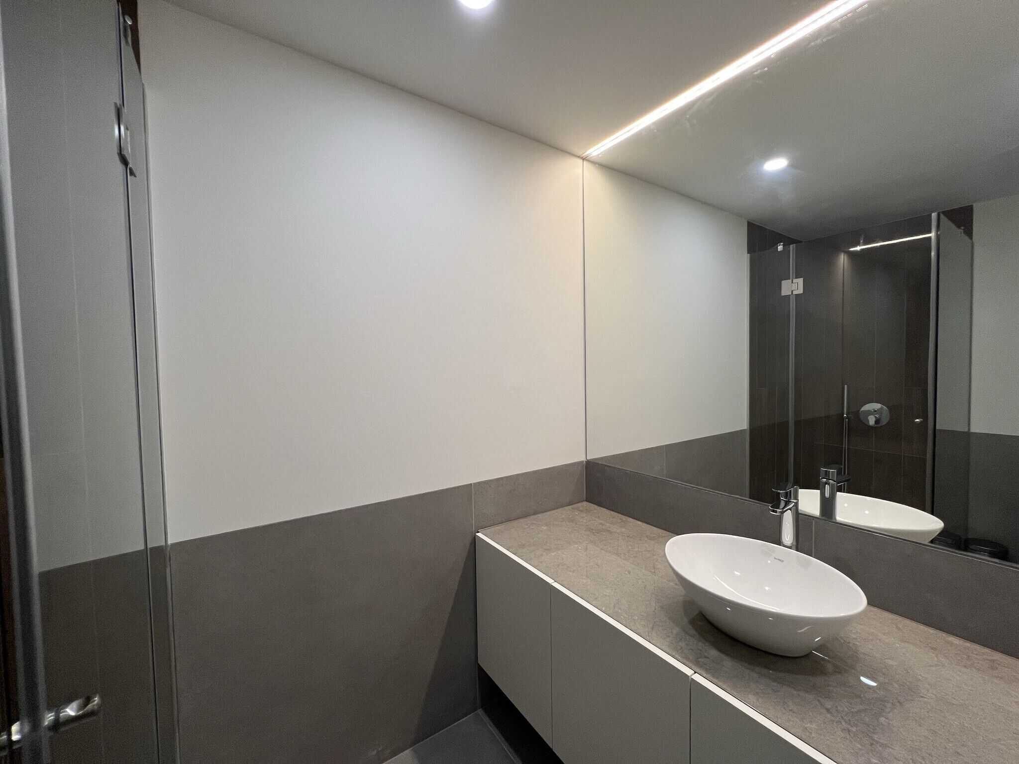 Uma casa de banho moderna com um espelho grande, uma sanita branca e zona de duche.