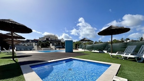 A swimming pool with a wooden deck, surrounded by artificial grass and white lounge chairs. - Albufeira Modern 2 by Homing (Albufeira)
