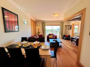 Ein modernes Hotelzimmer mit Essbereich, Wohnbereich mit Sofa und Sesseln, sowie ein Balkon mit Aussicht.