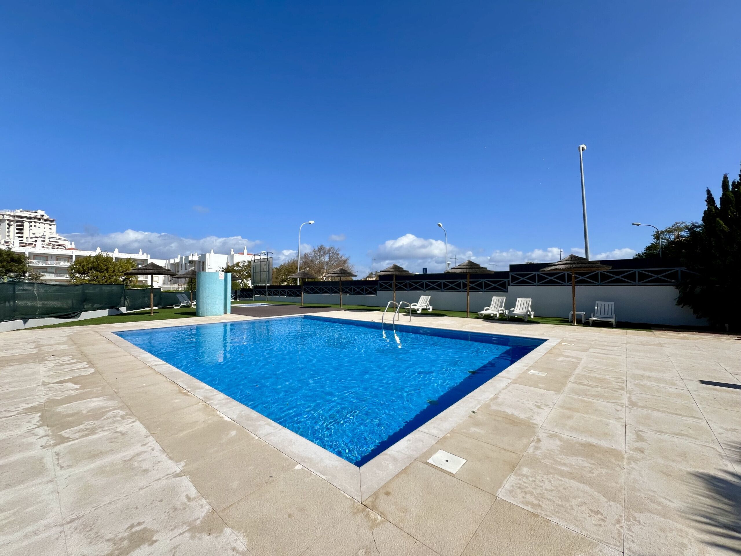 Une piscine rectangulaire à l’eau d’un bleu limpide, entourée d’une terrasse carrelée. Des chaises longues et des parasols sont disposés le long du bord de la piscine.