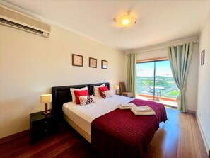 Ein Hotelzimmer mit einem großen Bett, einem Nachttisch, einer Lampe, einem Fenster mit Vorhängen und Blick auf die Stadt.