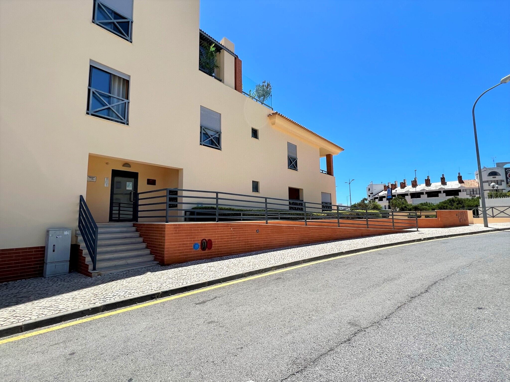 Un bâtiment moderne à la façade beige, avec un escalier menant à l’entrée et une zone pavée devant.