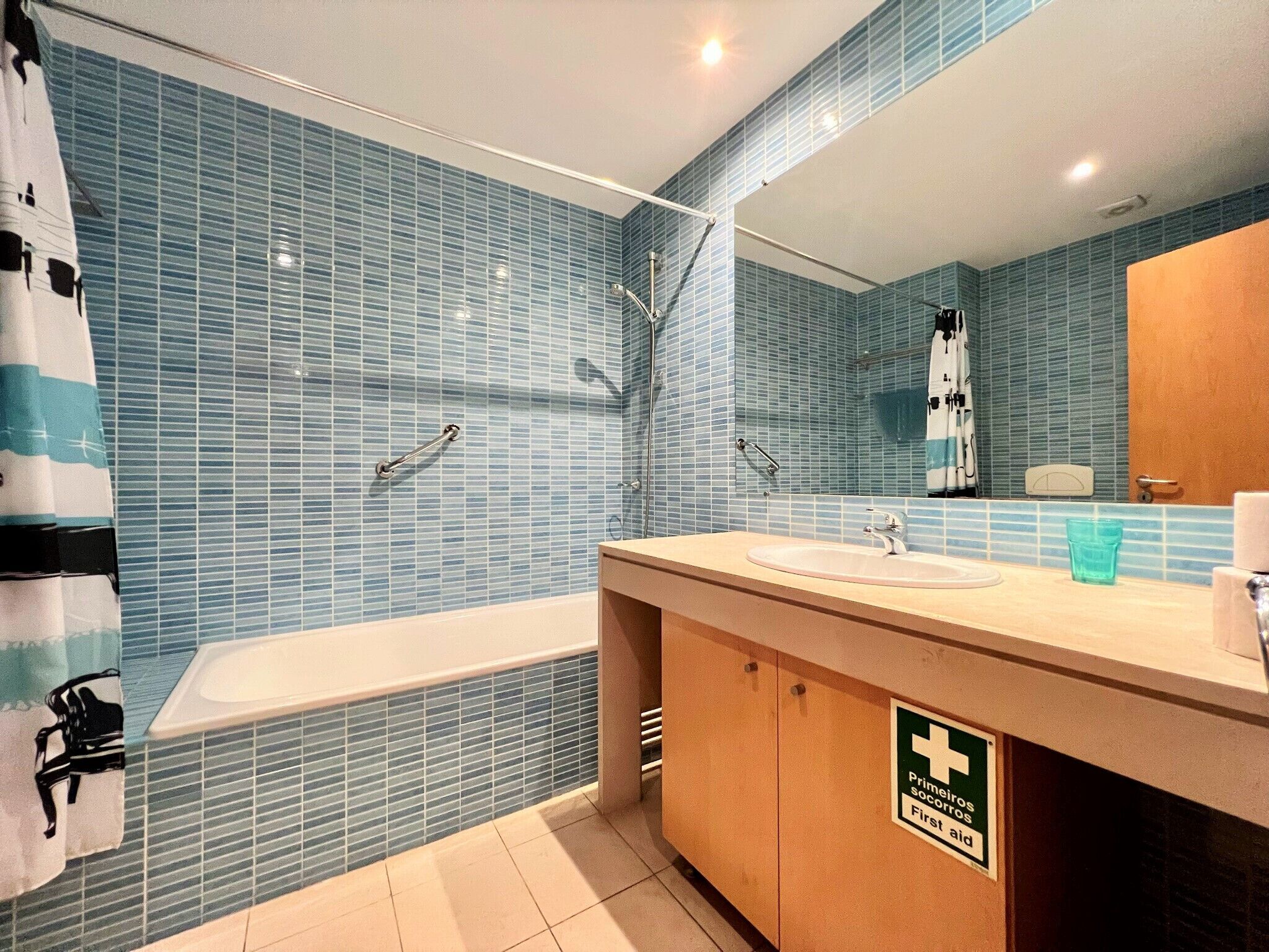 A bathroom with a bathtub, a sink, and a mirror. There is a sign indicating first aid availability.