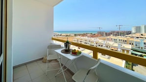 A balcony with a white table, two chairs, a bottle of champagne, and a fruit bowl. - Quarteira Panoramic View by Homing (Loulé)