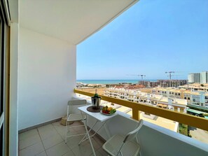 Ein Balkon mit einem weißen Tisch, zwei Stühlen, einer Champagnerflasche und einer Obstschale.