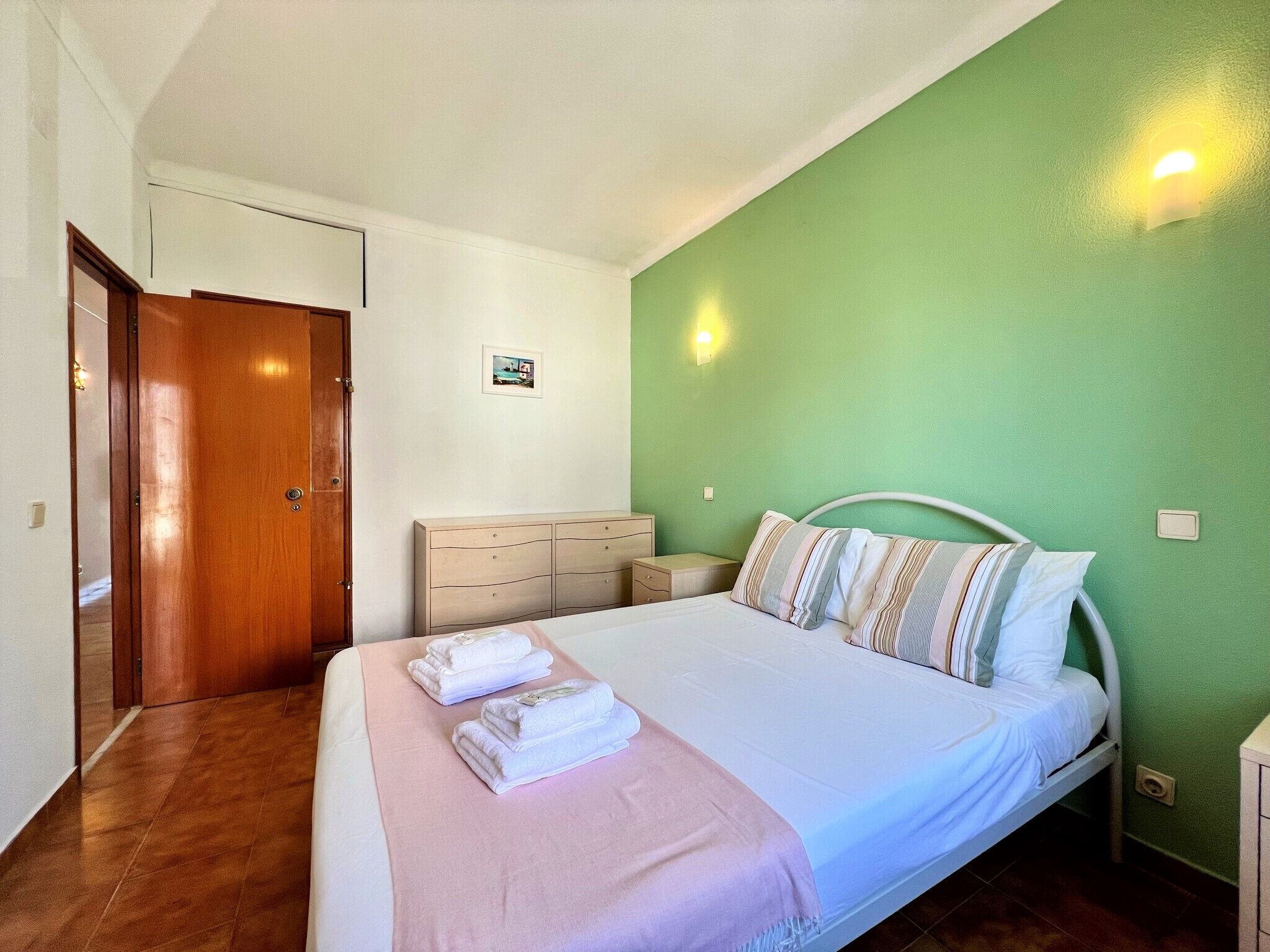 Une chambre à coucher avec un lit, une table de chevet, une commode et une porte.
