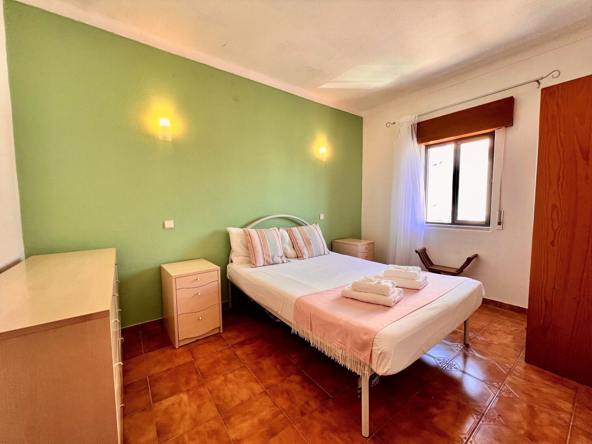 A bedroom with a bed, bedside tables, a chair, a window, and a door.