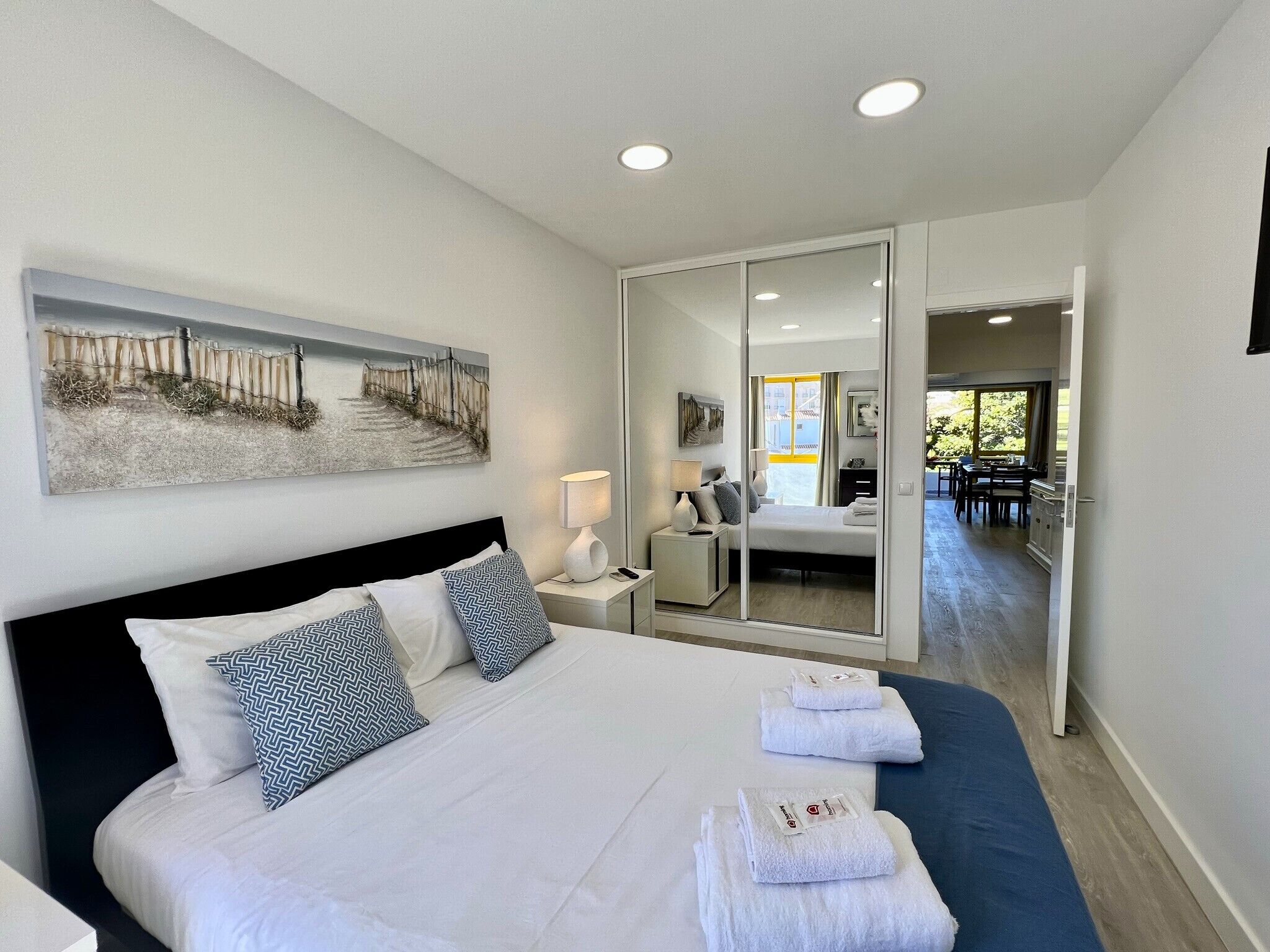 Camera d'albergo moderna con un letto grande, un comodino con una lampada, un quadro appeso al muro e vista sul'area ristorazione tramite una porta in vetro.