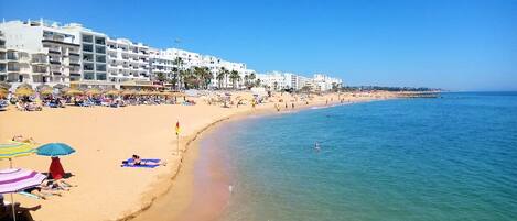 A beach with white buildings, clear blue water, and umbrellas.