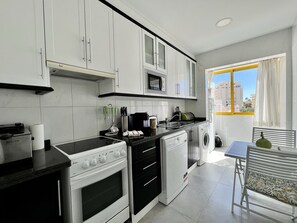 A modern kitchen with white cabinets, a black countertop, a built-in microwave, and a window with a yellow frame. - Quarteira Stylish With Pool by Homing (Loulé)