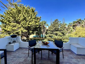 A patio with a table and chairs, a barbecue grill, and a view of a pool and trees. - Quarteira Stylish With Pool by Homing (Loulé)