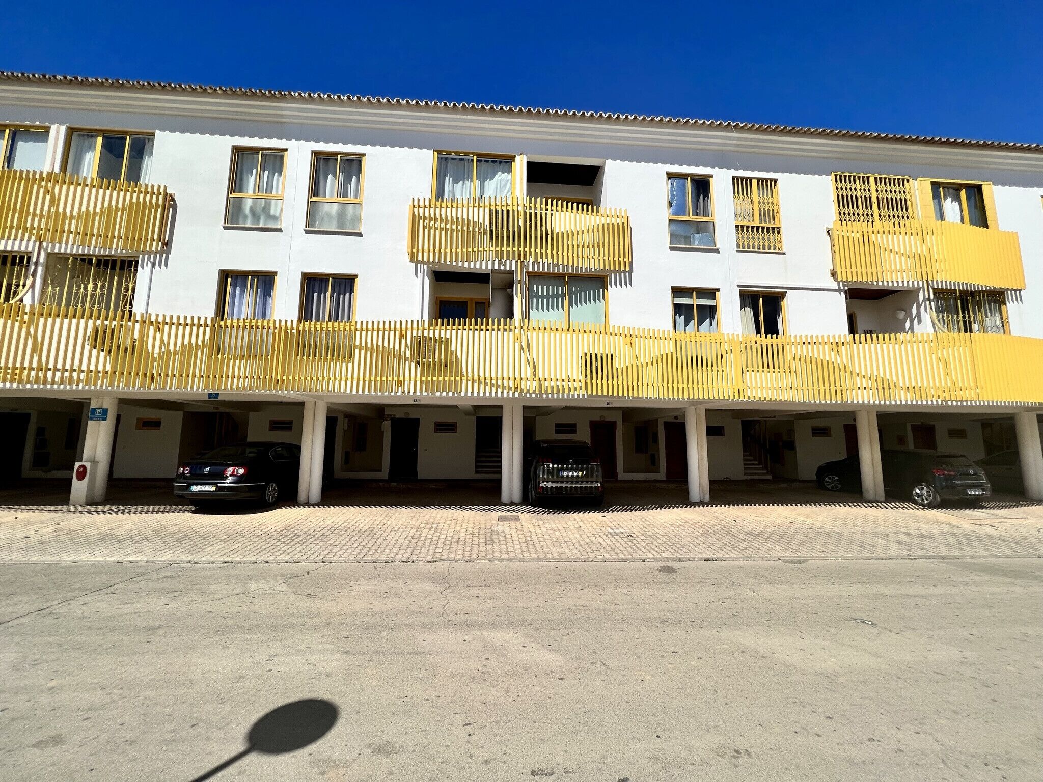 Un edificio de varios pisos con balcones, un área de estacionamiento y un cielo azul despejado.