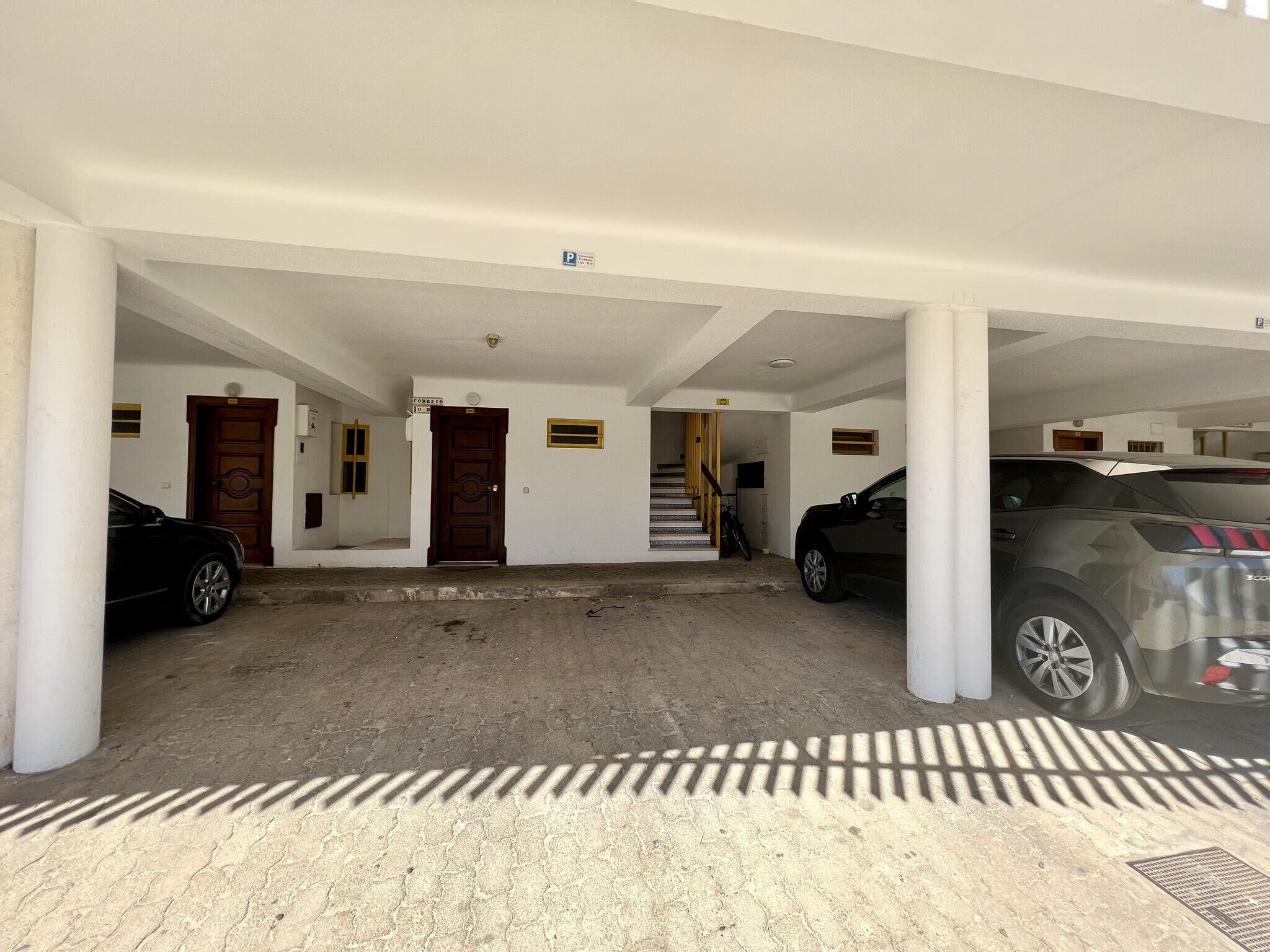 A covered parking area with two cars parked, a staircase leading to an upper level, and a door labeled "CÓBRETO".