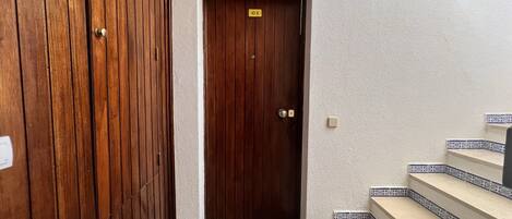 A wooden door with a 'Welcome' mat, a small sign above it, and a staircase with patterned tiles.