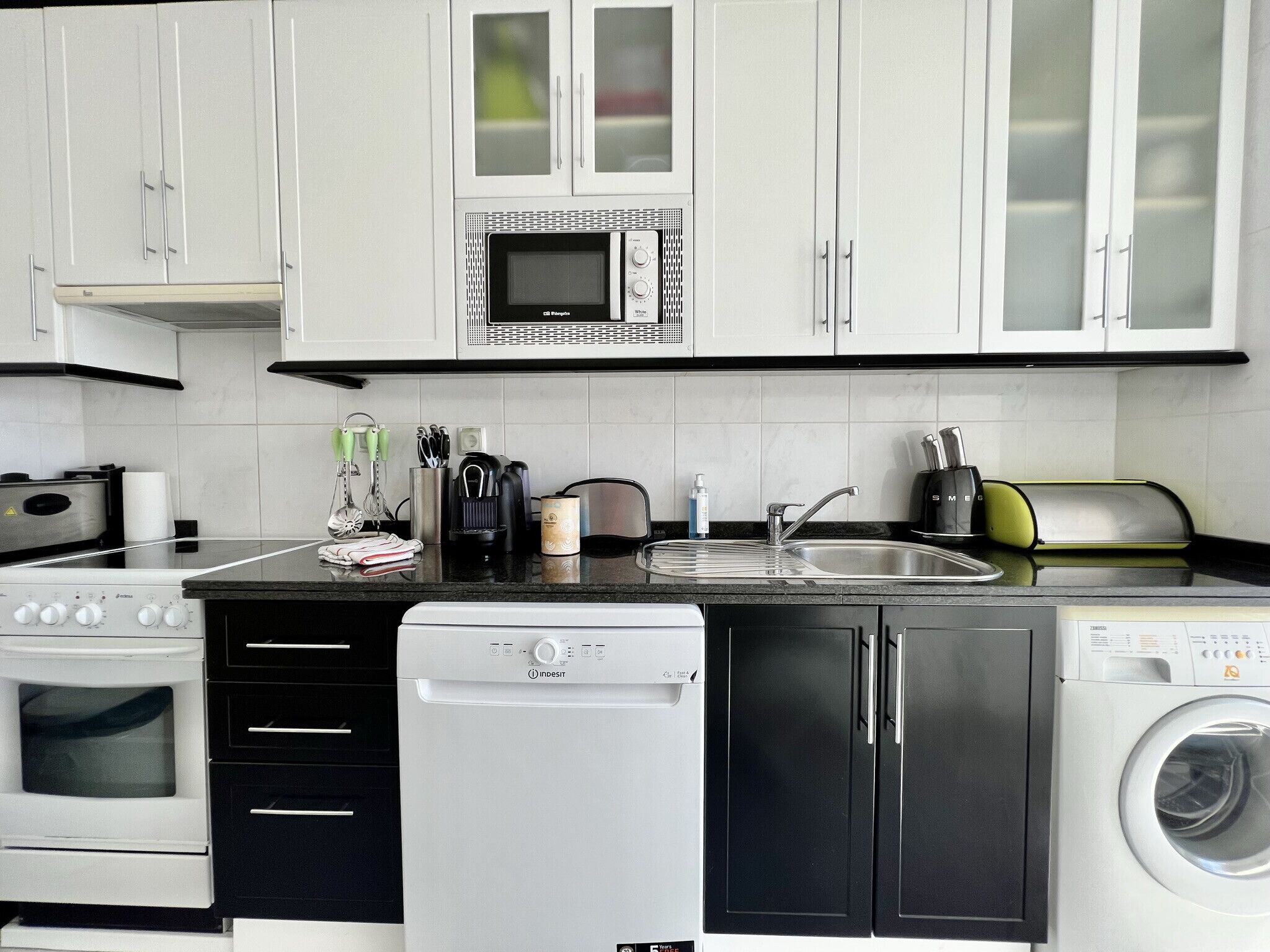 A modern kitchen with white cabinets, a built-in microwave, a dishwasher, and a washing machine.