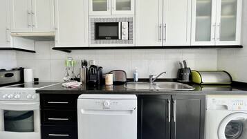Una cocina moderna con armarios blancos, microondas integrado, lavavajillas y lavadora.