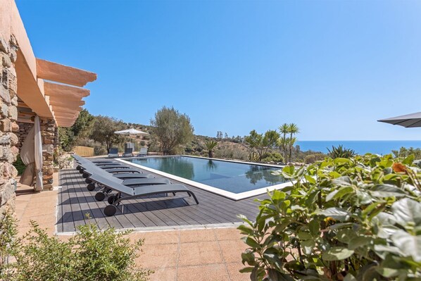 A swimming pool with a wooden deck, lounge chairs, and a stone wall. - Independent villa with five bedrooms and four bathrooms (Tertenia)