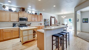 A spacious kitchen with wooden cabinets, a central island with stools, a large island sink, and a view to the dining area. - Pet-Friendly Meridian Vacation Rental w/ Fire Pit! (Meridian)